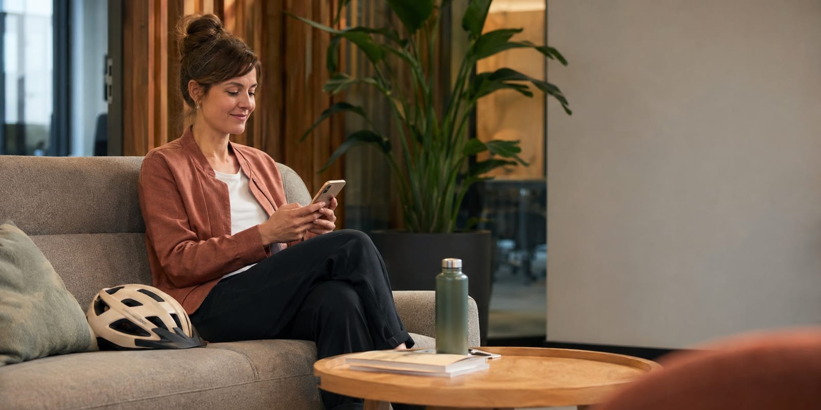Eine Frau sitzt entspannt auf einem Sofa und schaut lächelnd auf ihr Telefon.