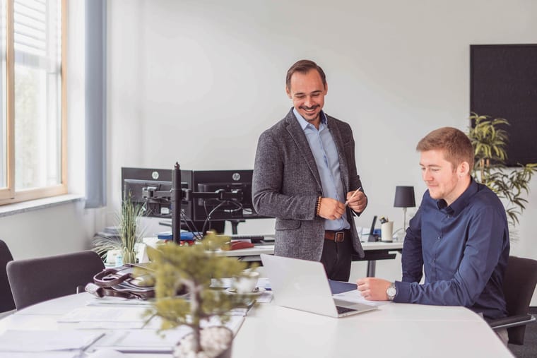 Zwei Kollegen besprechen im Büro Unterlagen am Laptop.
